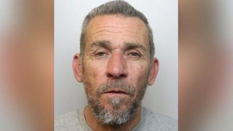 Mugshot of Gary Selwood. He has grey hair and a beard and is wearing a grey shirt.