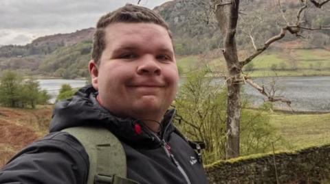 Archie Thompson stood outside with a tree, mountains and a lake in the background