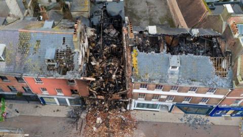 Gaping holes in roofs of terrace after fire - rubble from building in centre spills onto street.