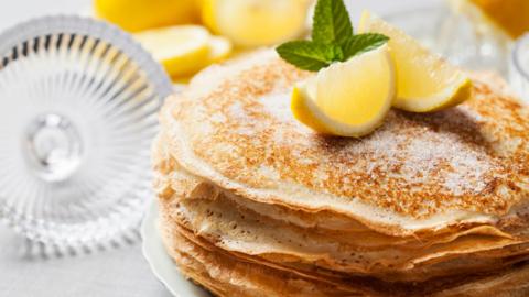 A pile of British-style pancakes with lemon slices and sugar on top