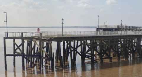 Google shot of the wooden pier. It has a safety railing around the walkway, a number of street lamps and a lifebuoy station.