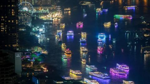 Boats lit up in a variety of colours cruise down the Chao Phraya river in Bangkok, Thailand