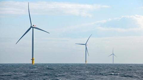 Three offshore wind turbines in the North Sea. Blue sky with clouds