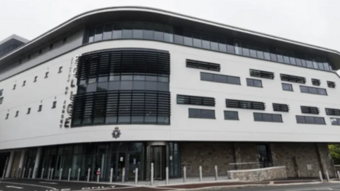 The outside of the Jersey police building in St Helier, a white building with rectangular dark glass windows around the top and sides. 
