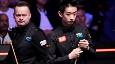 Wu Yize and Shaun Murphy look at the table
