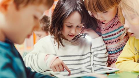 A group of young children gather round a ipad