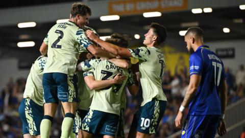 Cardiff City players celebrate in a huddle in front of dejected AFC Wimbledon player Marcus Browne