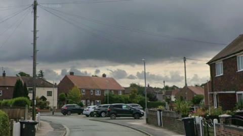 Image shows a street on a housing estate made up of mid-20th century council housing.