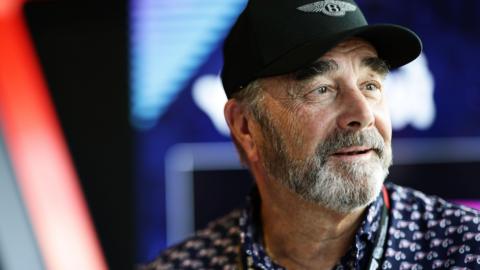 Nigel Mansell is wearing a black cap and a patterned navy shirt, and looks off to the side of the camera.