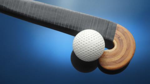 Close-up of white hockey ball and wooden stick on blue background