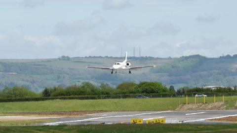 A small white plan landing at Gloucestershire Airport.
