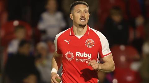 Ronan Coughlan running looking forward in a night game, wearing club's home red and white kit