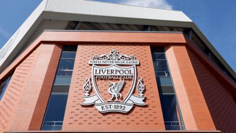 A view of the exterior of Anfield Stadium, including metal signage showing the club's crest