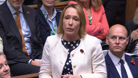 A woman with blonde hair, a blue and white spotted top and a pale jacket standing in the House of Commons