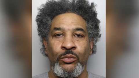 A mugshot of a man with a beard
