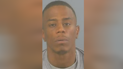 A mugshot of Donovan Thomas, who is wearing a grey sweatshirt and grey T-shirt 