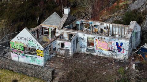 An aerial view of the cottage. The roof is missing and the walls are covered in graffiti. 