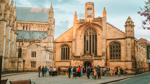 Exterior of St Michael le Belfrey Church, next to York Minster, with crowds of people in front of the building