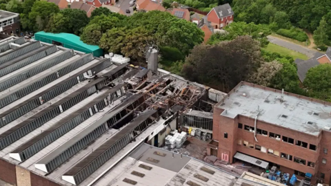 A picture taken with a drone, showing part of the fire-damaged factory, with homes behind it, divided by trees.