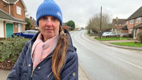 A woman with a blue woollen hat, a pink scarf and a blue coat with a long road stretching off into the distance