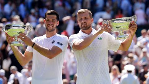 Julian Cash (L) and Lloyd Glasspool (R) smile as they hold up their Wimbledon trophies.
