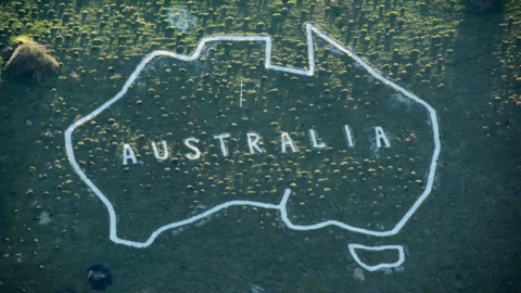 A grassy hillside with the white outline of a map with the word 'Australia' in the middle