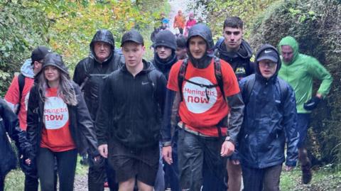 A number of people taking part in the climb walking down a path in the pouring rain.