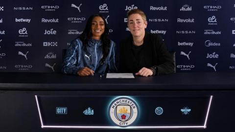 New Manchester City signing Kerolin sat at a desk with women's director of football Therese Sjogran 