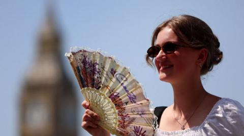 A woman uses a fan in London during a late-June heatwave