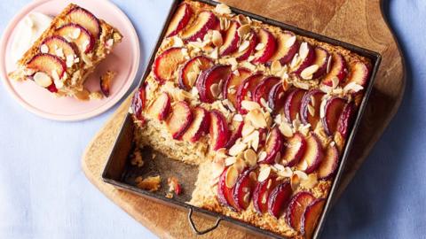 A large metal tray of plum and almond baked oats, resting on a wooden cutting board.