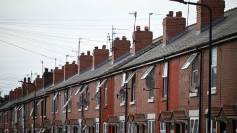 Terraced houses in Eastwood. They are all plain redbrick with identical white window frames, small covered porches, tiled roofs and brick chimneys.