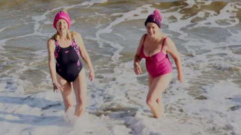 Two women in swimming costumes and woolly hats in the sea 