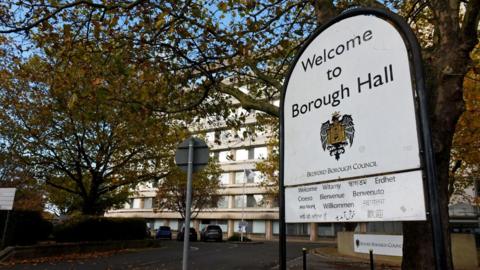 Bedford Borough Council's headquarters. There is a white building in the background and in the foreground is a white sign that says "Welcome to Borough Hall".