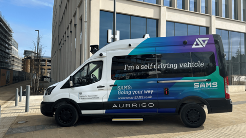 A multi-coloured van which says "I'm a self driving vehicle" on the side.