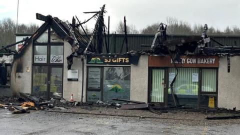 The retail units have lost their roofs and there is debris on the ground.