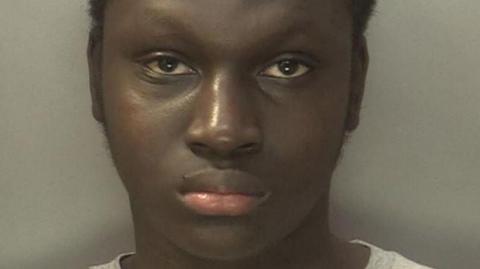 Oumar is staring at the camera and has short, dark hair and a grey top on.
