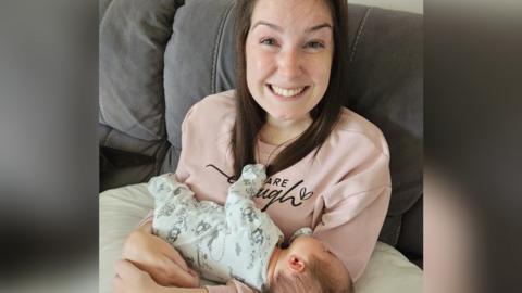 Lucy Lintott Smith holds her sleeping baby who is supported on a pillow