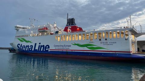 The Stena Vinga ferry is pictured in St Helier marina in Jersey. It is a white vessel and a red lifeboat is attached to the side. The words Stena Line Connecting Europe for a Sustainable Future are written on the side in blue.
