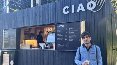 Emanuele Pecorari stood with a cup of coffee outside the Ciao coffee kiosk, which has black wood panelling 