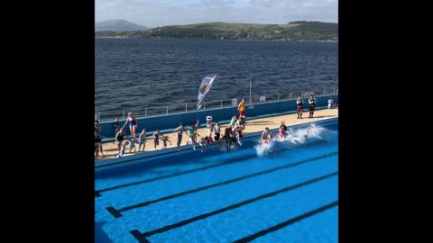Water splashes as swimmers jump into an outdoor swimming pool