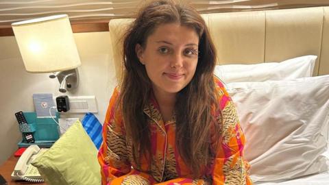 A woman sits on a bed smiling
