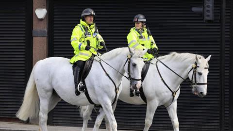 Two Stockport officers in uniform on two white police horses, riding through Stockport town centre