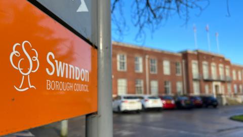 Orange Swindon Borough Council sign with offices in the background