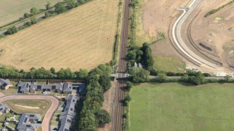A birds-eye view of the Cross Lane crossing in Collingham. There are houses, fields, and a railway line.