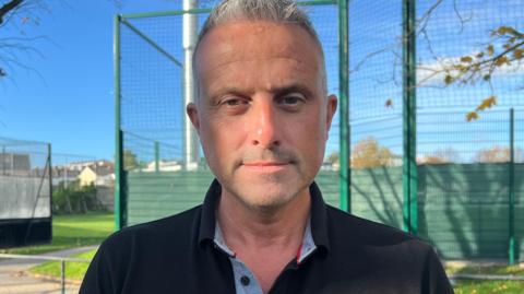 Carl Walker is looking into the camera. He has short grey hair and is wearing a black polo shirt.