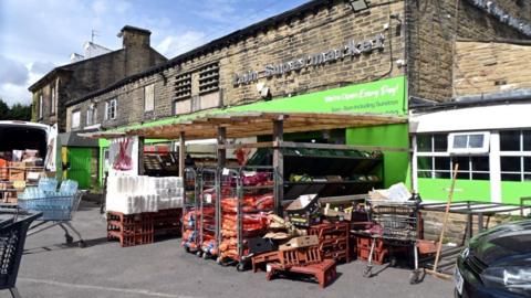 A building which has been converted into a supermarket with bright green signs at the front and rows of palets containing produce. 