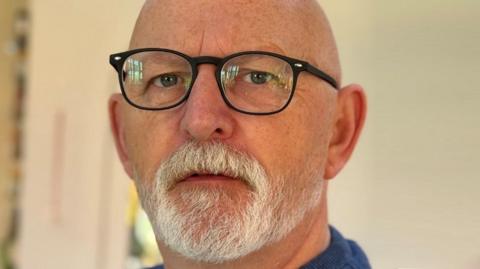 A close-up of a man with a white beard and glasses.