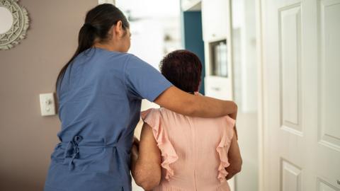 Care home scene - worker is helping older woman towards a doorway