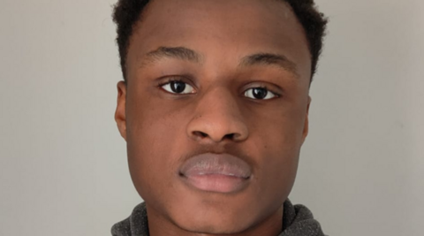 Michael Ababio, with dark hair, is looking at the camera. He is pictured in front of a grey background.