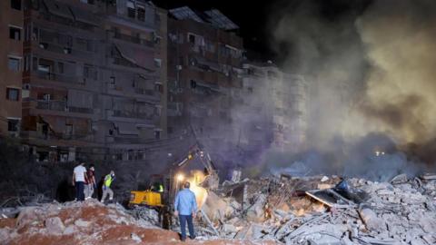 People inspect damage at the site of an Israeli strike in Dahiyeh